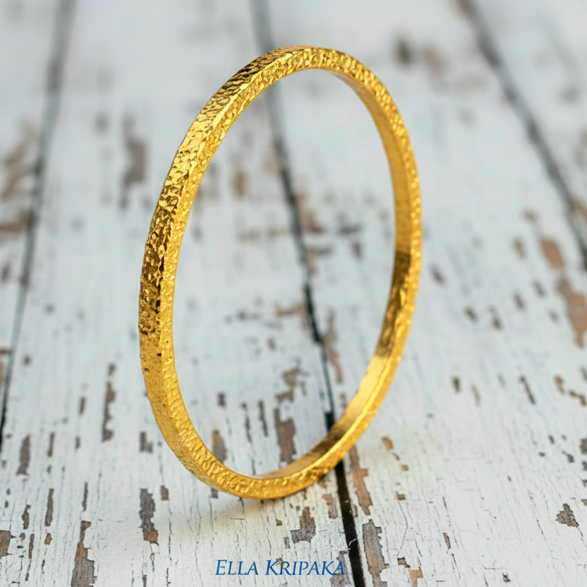 Hammered 24k 9999 gold bangle thick bracelet Ancient Rome style on a white wooden background, artist-jeweler name 'Ella Kripaka'