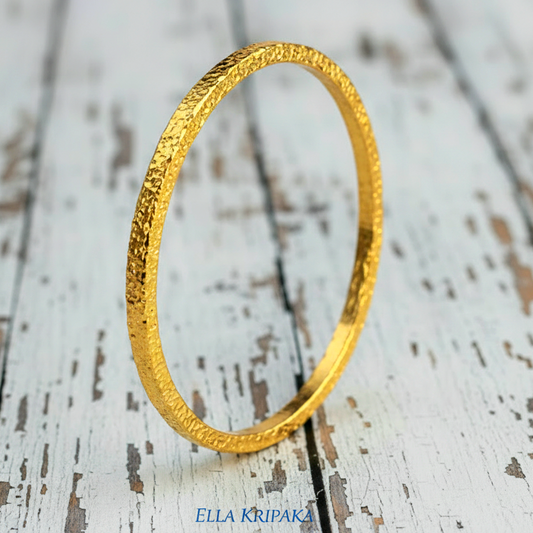 Hammered 24k 9999 gold bangle thick bracelet Ancient Rome style on a white wooden background, artist-jeweler name 'Ella Kripaka'