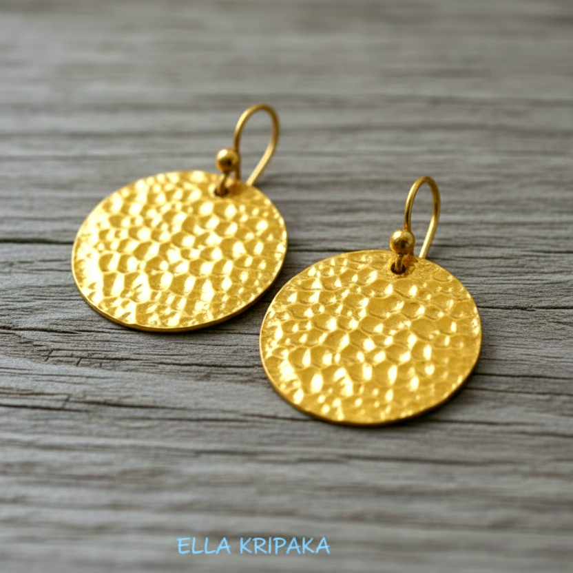Organic ammered 24k gold, pure 9999 gold disk earrings with shiny forged gold textures on old wooden surface, artist-jeweler 'Ella Kripaka' branding