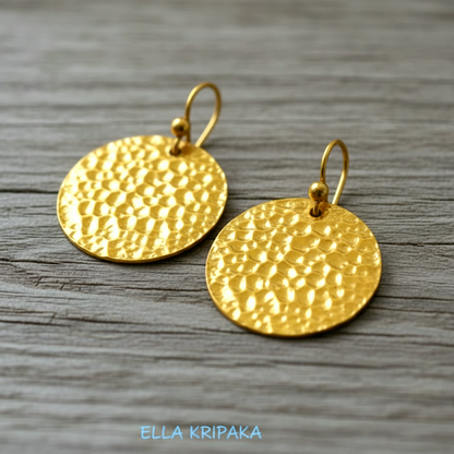 Organic ammered 24k gold, pure 9999 gold disk earrings with shiny forged gold textures on old wooden surface, artist-jeweler 'Ella Kripaka' branding