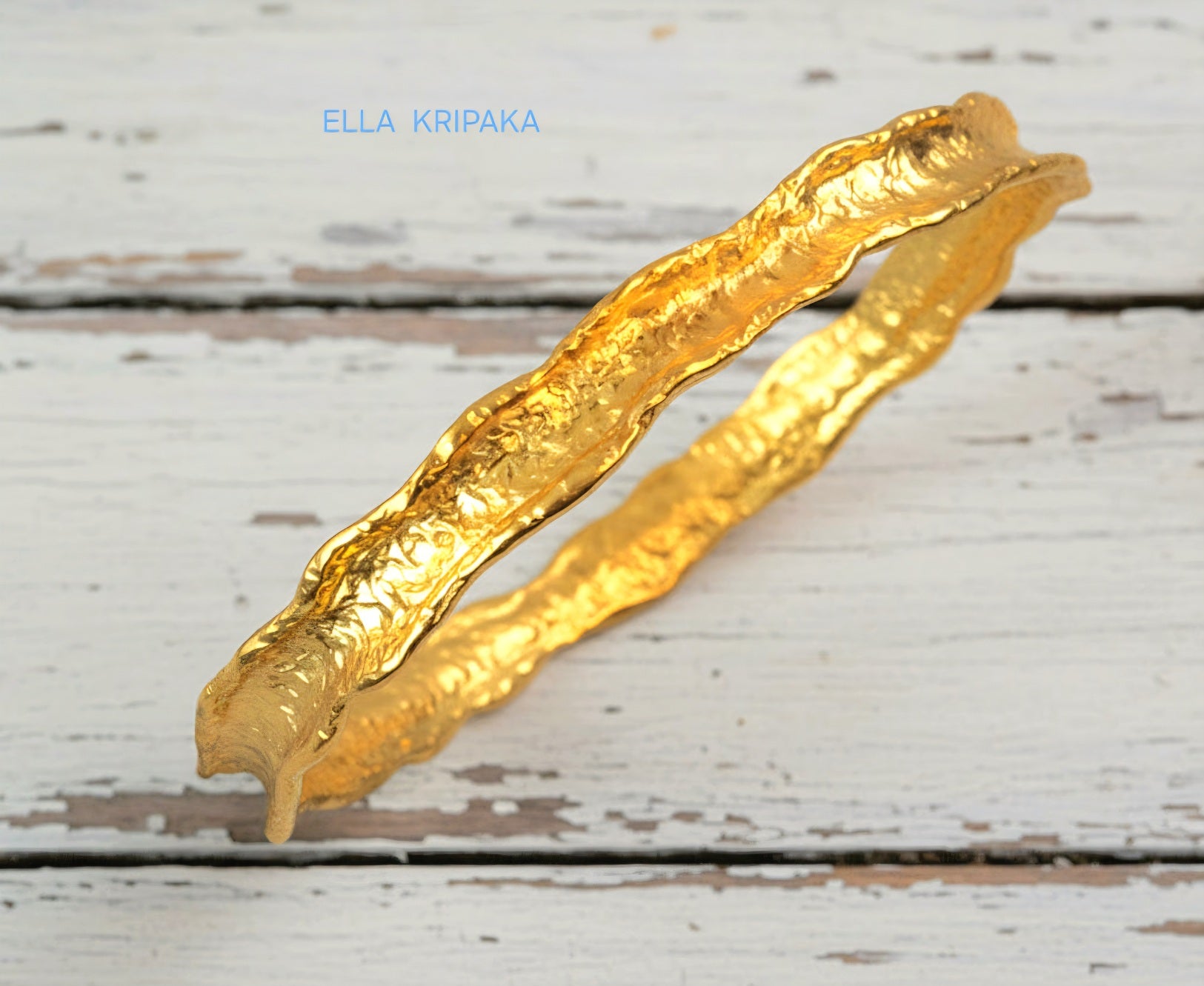 Hammered 22k gold organic textured bangle bracelet with uneven edges on old white wooden surface with 'Ella Kripaka' branding