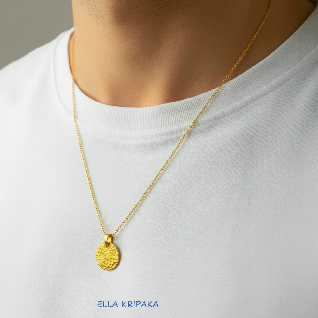 Hammered 24k gold, pure 9999 gold disk pendant on chain worn by a man and with white t-shirt and on grey background, artist-jeweler 'Ella Kripaka' branding