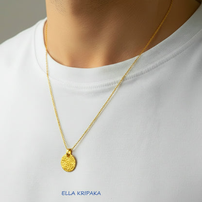 Hammered 24k gold, pure 9999 gold disk pendant on chain worn by a man and with white t-shirt and on grey background, artist-jeweler 'Ella Kripaka' branding