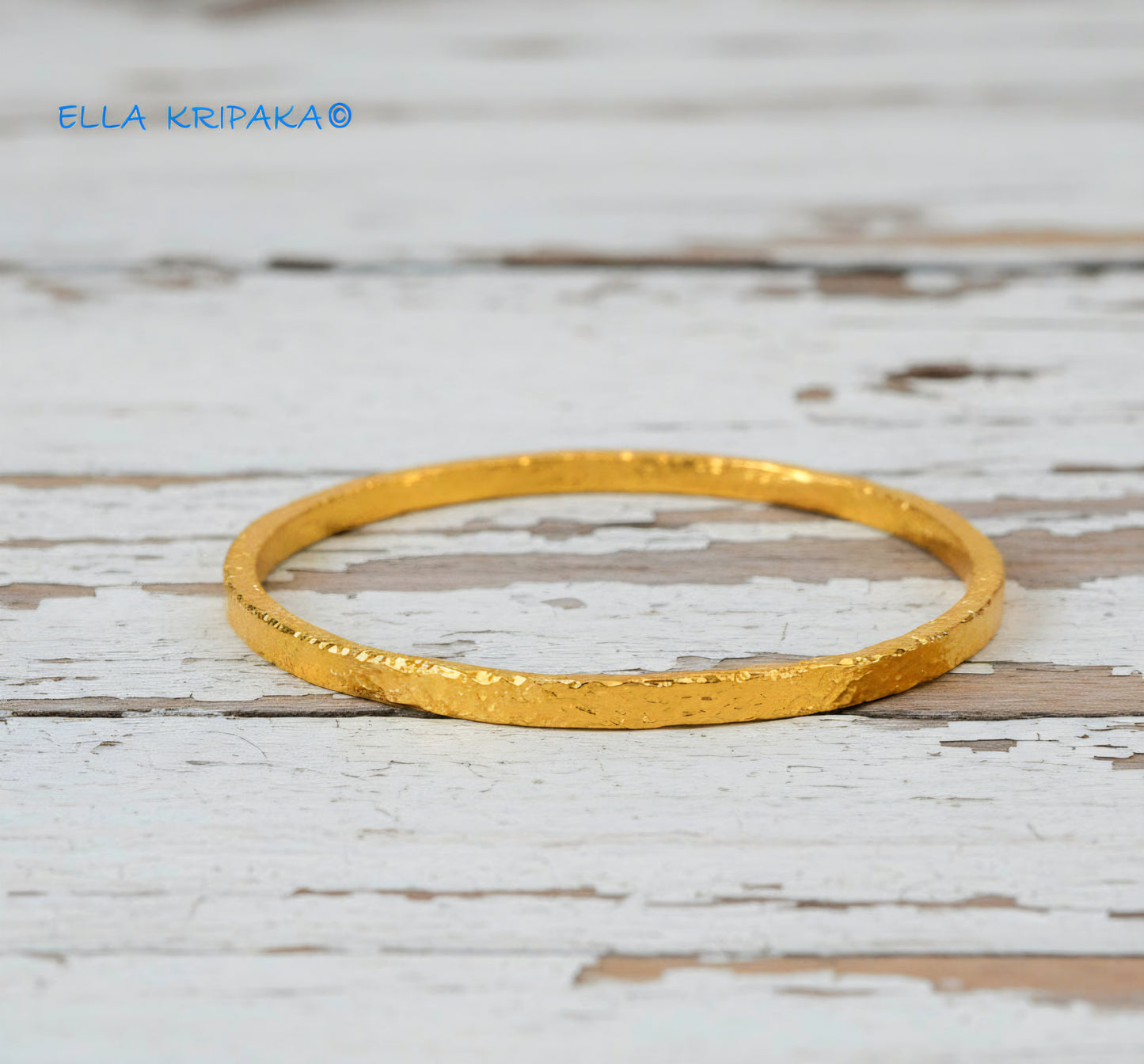 Hammered 24k 9999 gold bangle thick bracelet Ancient Rome style on a white wooden background, artist-jeweler name 'Ella Kripaka'