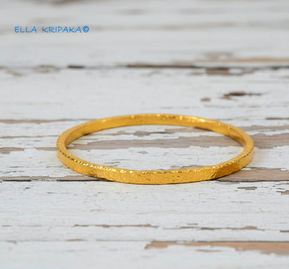 Hammered 24k 9999 gold bangle thick bracelet Ancient Rome style on a white wooden background, artist-jeweler name 'Ella Kripaka'