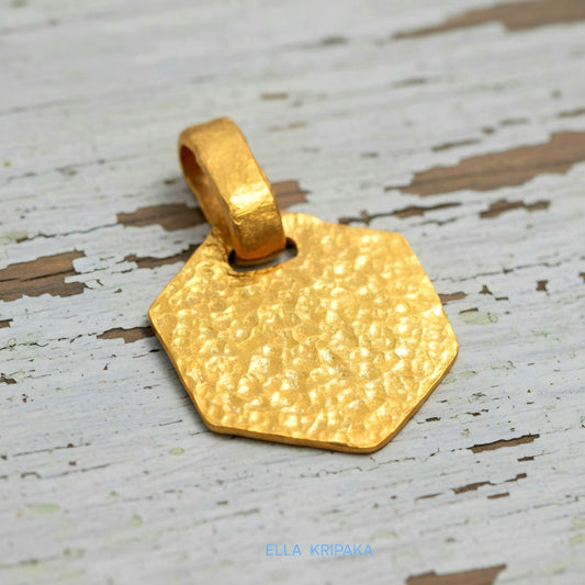 Hammered 24k gold, pure 9999 gold hexagon pendant with shiny forged gold textures on white old wooden surface, artist-jeweler 'Ella Kripaka' branding