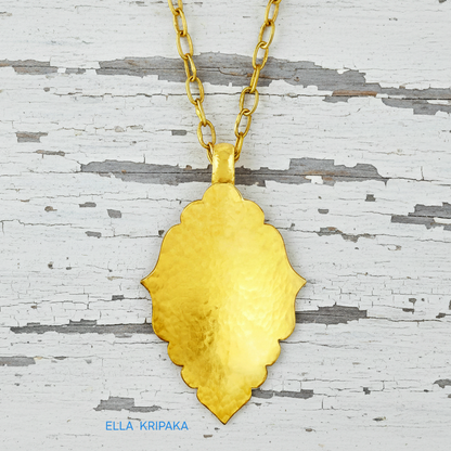 Hammered 24k gold Byzantine ornament pendant with thick chain on a white rustic wooden surface with 'Ella Kripaka' branding