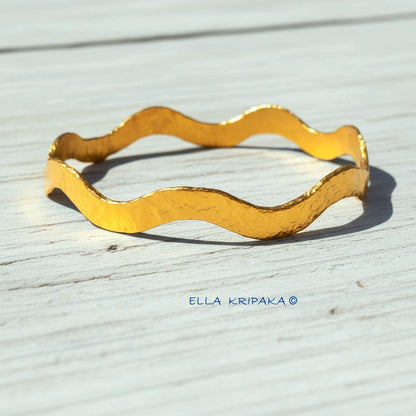 24k gold hammered bracelet thick bangle with wavy design on white rustic wooden background, branded 'Ella Kripaka'