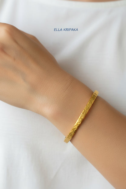 Hammered 24k 9999 gold bangle thick bracelet Ancient Rome style worn by a woman on hand and a white t-shirt background, artist-jeweler name 'Ella Kripaka' branding