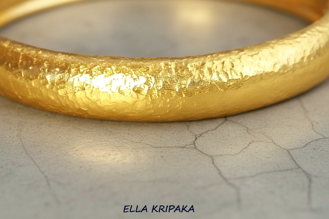 Hammered 24k gold bangle thick bracelet with  10mm of width and with gold textures on grey concrete background, and artist-jeweler 'Ella Kripaka' branding