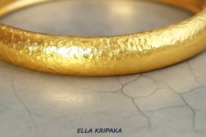 Hammered 24k gold bangle thick bracelet with  10mm of width and with gold textures on grey concrete background, and artist-jeweler 'Ella Kripaka' branding