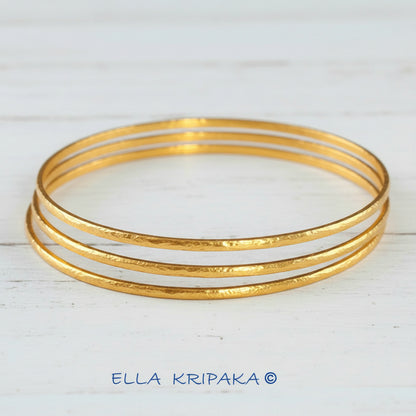 Hammered 22k gold three textured bangles bracelets Ancient Rome style on white wooden surface with 'Ella Kripaka' branding