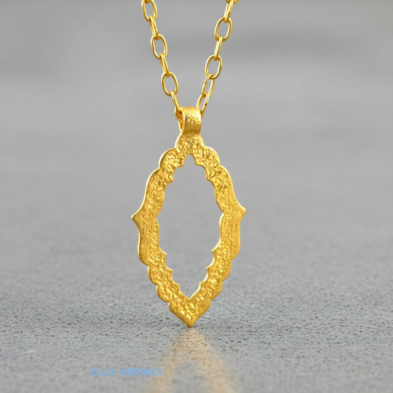 Hammered 24k gold Byzantine ornament pendant wuth a chain on a grey concrete surface with 'Ella Kripaka' branding