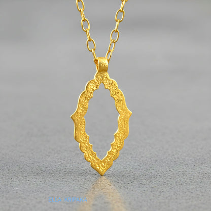 Hammered 24k gold Byzantine ornament pendant wuth a chain on a grey concrete surface with 'Ella Kripaka' branding