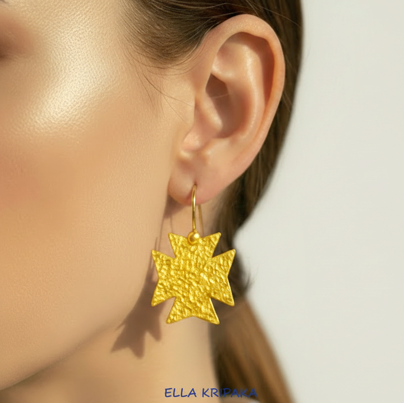 Hammered 24k gold, pure 9999 gold Byzantine cross earring with shiny forged gold textures worn on a woman and with light grey background, artist-jeweler 'Ella Kripaka' branding