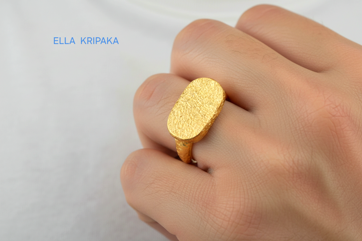 Hammered 24k Gold 9999 gold signet thick ring Ancient Rome style with textured gold worn on person's finger and on a white blurred background, branded 'Ella Kripaka'