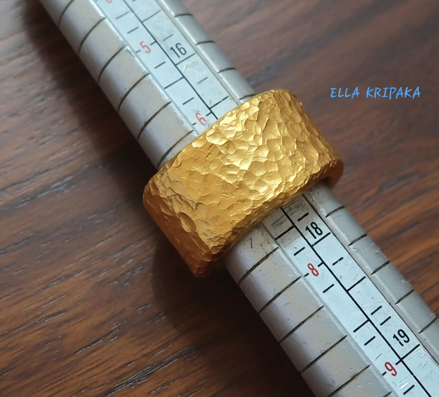 Hammered 24k 9999 Gold thick ring organic with textured gold on ring mandrel jewelry tool on a dark wooden surface, branded 'Ella Kripaka'