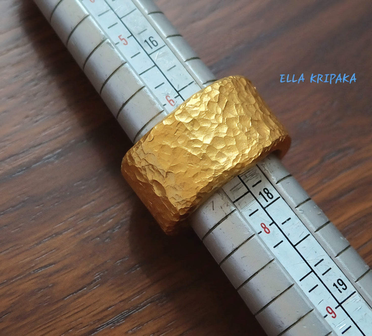 Hammered 24k 9999 Gold thick ring organic with textured gold on ring mandrel jewelry tool on a dark wooden surface, branded 'Ella Kripaka'