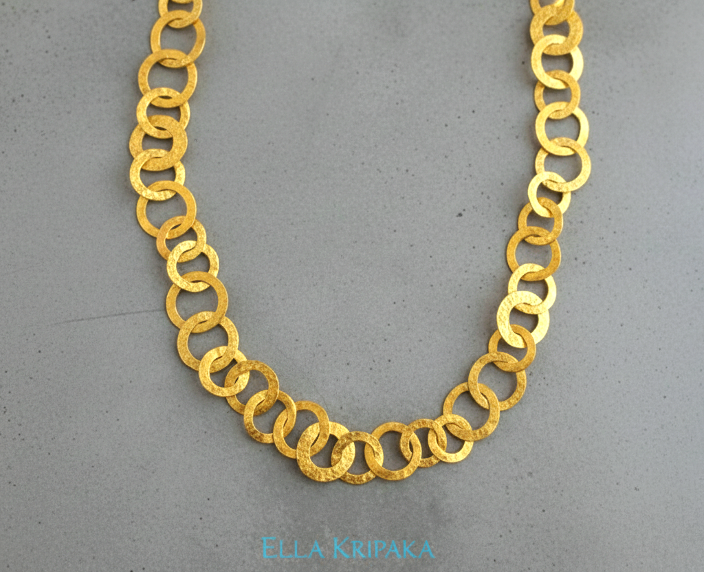 22k gold hammered chain necklace with different links on a grey concrete surface, and with 'Ella Kripaka' branding