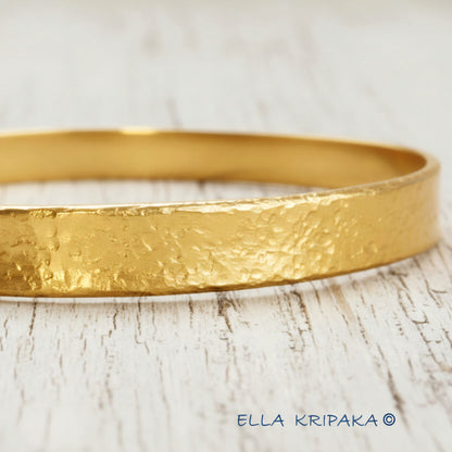 24k 9999 gold hammered Ancient Rome style bracelet bangle on white rustic wooden surface, indicating it is a custom-made jewelry with creator's name 'Ella Kripaka'