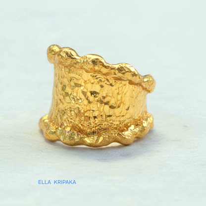 Organic hammered 24k 9999 Gold ring signet with uneven wavy thick edges on white old wooden surface, artist-jeweler's name 'Ella Kripaka' is written in picture
