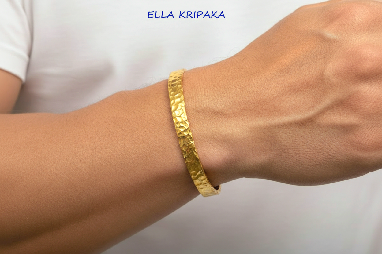 Organic hammered 24k gold bracelet cuff with uneven edges and textured design is worn by a man on wrist and on light blurred background, branding artist 'Ella Kripaka'