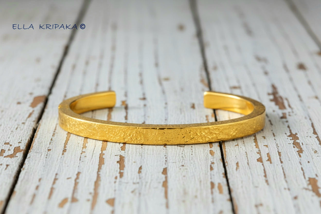 Hammered 24k 9999 gold cuff thick bracelet Ancient Rome style on an old white wooden background, artist-jeweler name 'Ella Kripaka' branding