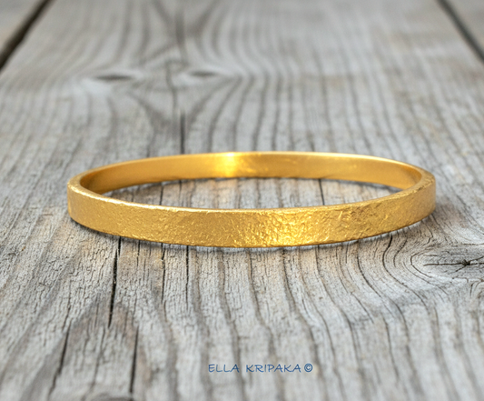 Hammered 24k 9999 gold bangle thick bracelet Ancient Rome style on an old wooden background, artist-jeweler name 'Ella Kripaka' branding