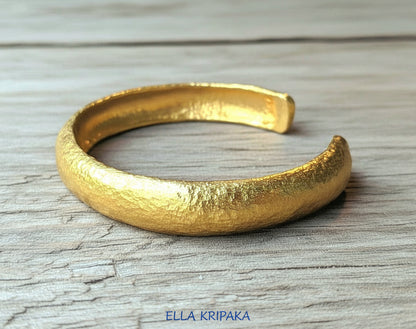 24k 9999 gold hammered Ancient Rome style bracelet cuff on old wooden background, indicating it is a custom-made jewelry with creator's name 'Ella Kripaka'
