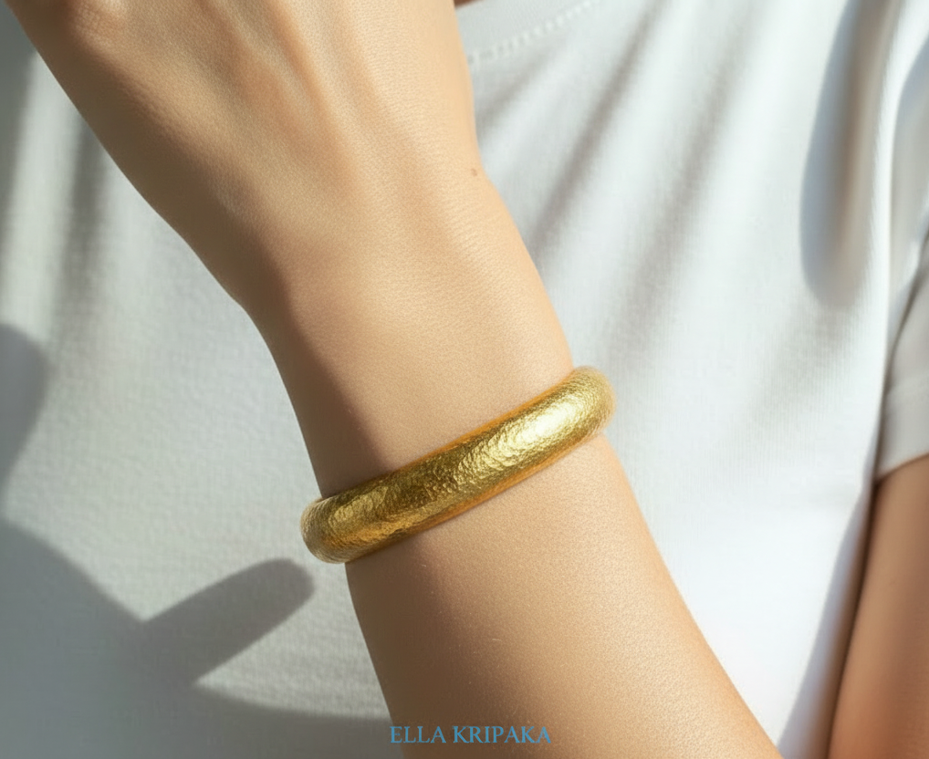 24k 9999 gold hammered Ancient Rome convex bracelet cuff worn on woman's wrist with a white t-shirt background, indicating it is a custom-made jewelry with creator's name 'Ella Kripaka'