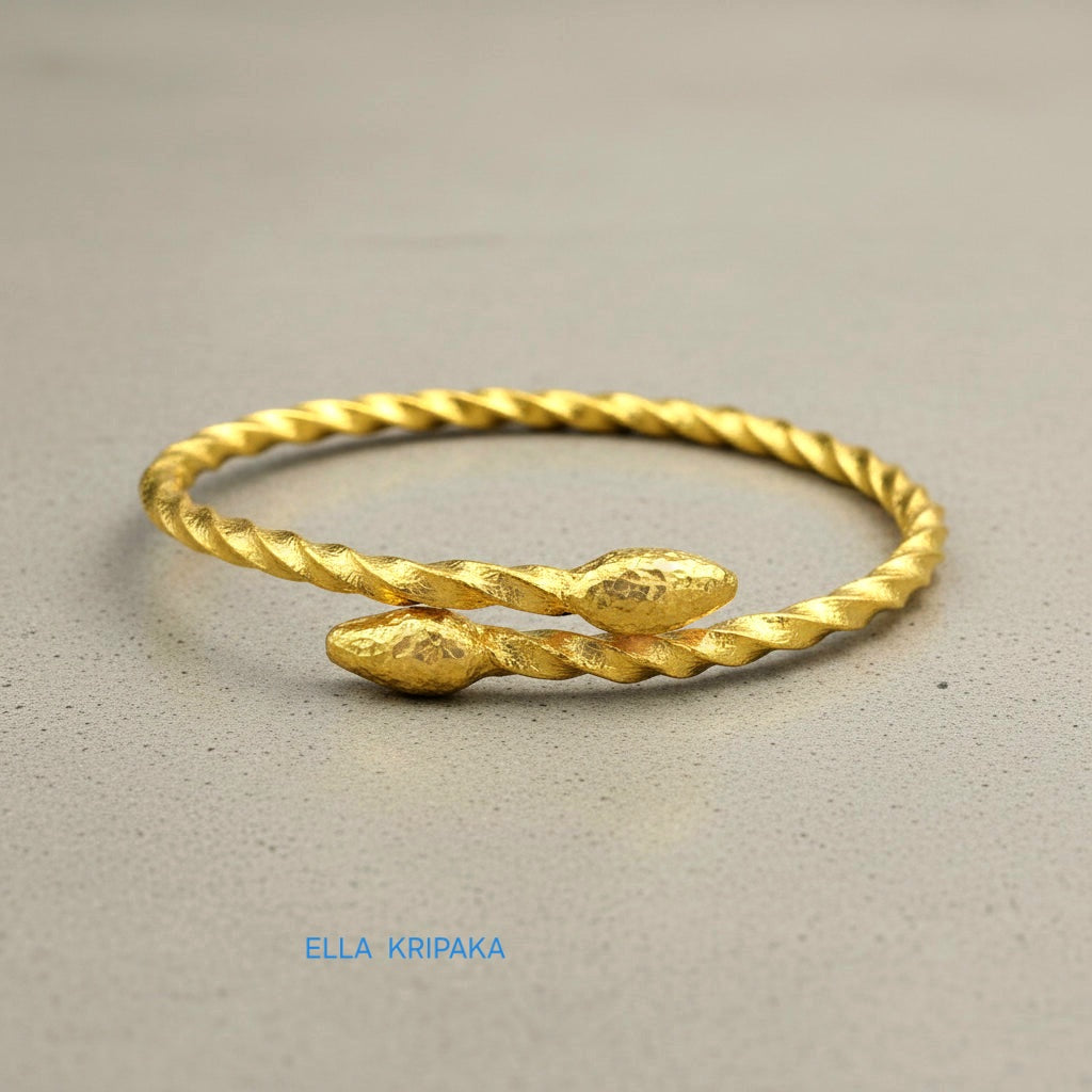 Twisted 24k gold hammered bracelet with thick oval ends and with textured design on grey concrete surface, branded artist-jeweler 'Ella Kripaka'
