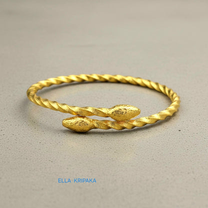 Twisted 24k gold hammered bracelet with thick oval ends and with textured design on grey concrete surface, branded artist-jeweler 'Ella Kripaka'