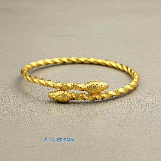 Twisted 24k gold hammered bracelet with thick oval ends and with textured design on grey concrete surface, branded artist-jeweler 'Ella Kripaka'