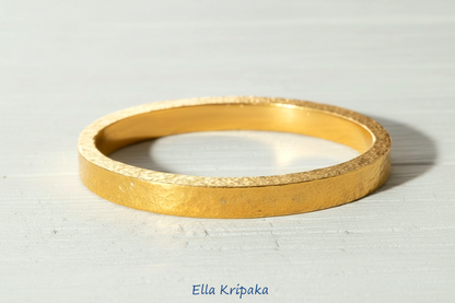 Hammered 24k 9999 gold bangle thick bracelet Ancient Rome style on a white old wooden background, artist-jeweler name 'Ella Kripaka' branding