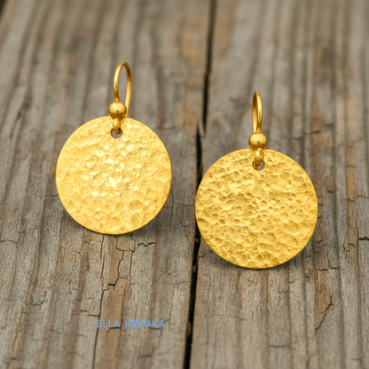 Hammered 24k gold, pure 9999 gold disk earrings with shiny forged gold textures on old wooden surface, artist-jeweler 'Ella Kripaka' branding