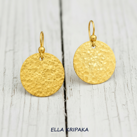 Hammered 24k gold, pure 9999 gold disk earrings with shiny forged gold textures on old wooden surface, artist-jeweler 'Ella Kripaka' branding