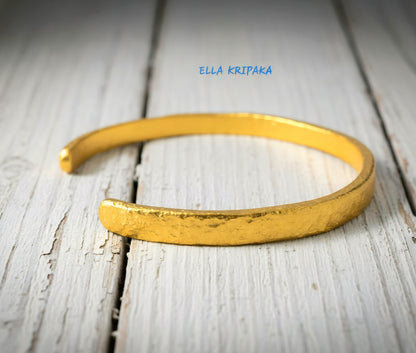 Hammered 24k 9999 gold cuff thick bracelet Ancient Rome style on an old white wooden background, artist-jeweler name 'Ella Kripaka' branding