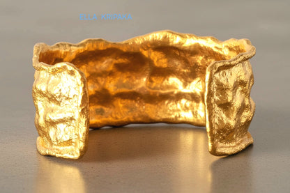 Organic 24k gold hammered bracelet cuff with a textured surface on a grey concrete background, branded 'Ella Kripaka'