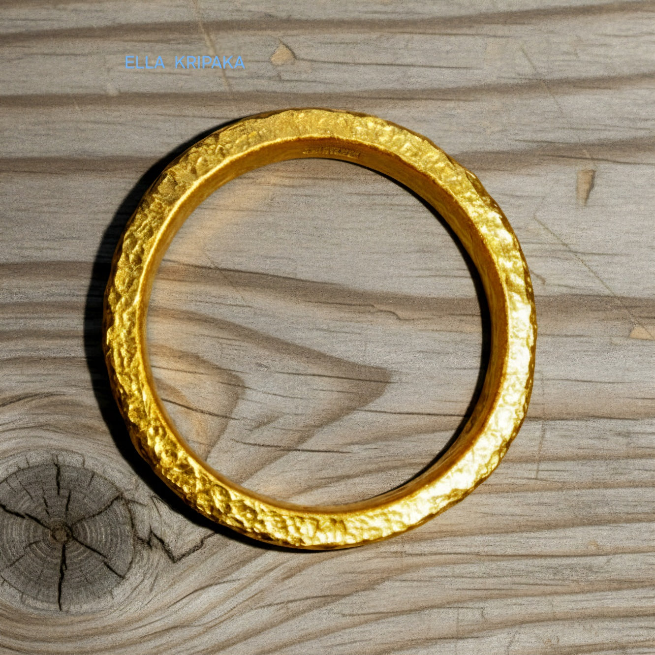 Hammered 24k gold thick ring on rustic wooden surface, artist-jeweler's name 'Ella Kripaka' is branded