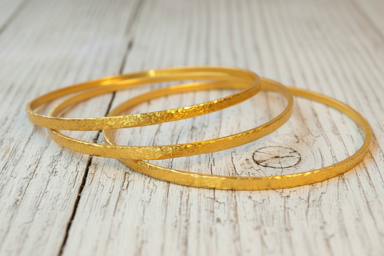 Hammered 22k gold three textured bangles bracelets Ancient Rome style on old wooden surface with 'Ella Kripaka' branding