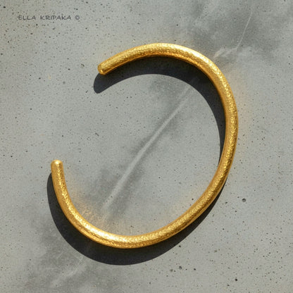 Hammered 24k 9999 gold cuff thick bracelet Ancient Rome style on a grey background, artist-jeweler name 'Ella Kripaka' branding