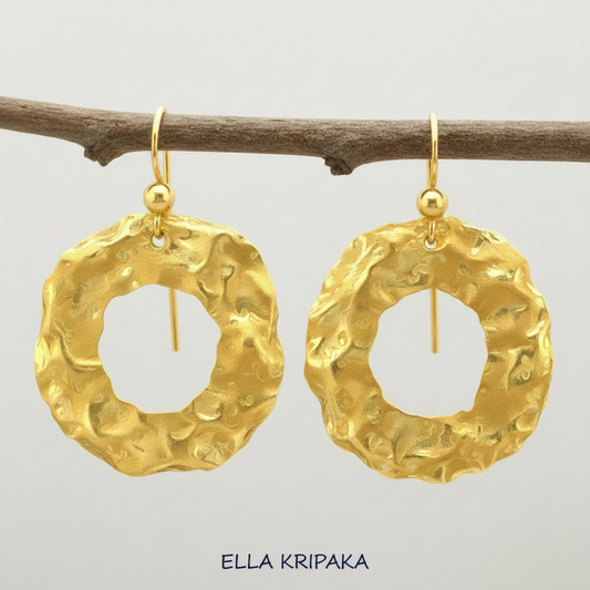Organic 24k gold hammered wavy hoops earrings with shiny uneven gold textures are hanging on branch and on light grey background, artist-jeweler 'Ella Kripaka' branding