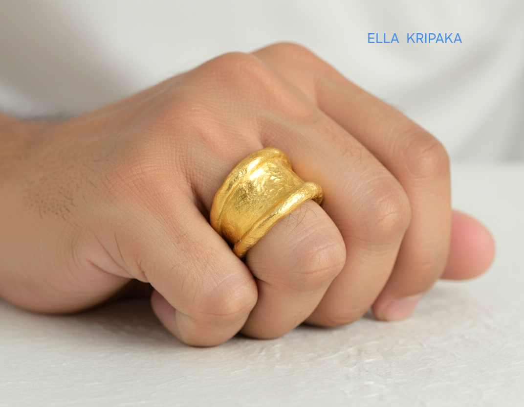 Organic hammered 24k Gold 9999 gold ring signet with thick edges and with textured surface on person's finger on a blurred background, branded 'Ella Kripaka'