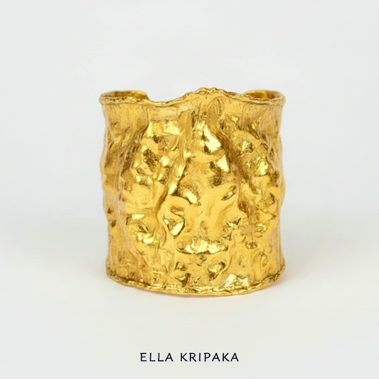 Hammered 24k gold large cuff bracelet with convex uneven textures and with 65 mm of width on a white background, and with 'Ella Kripaka' branding
