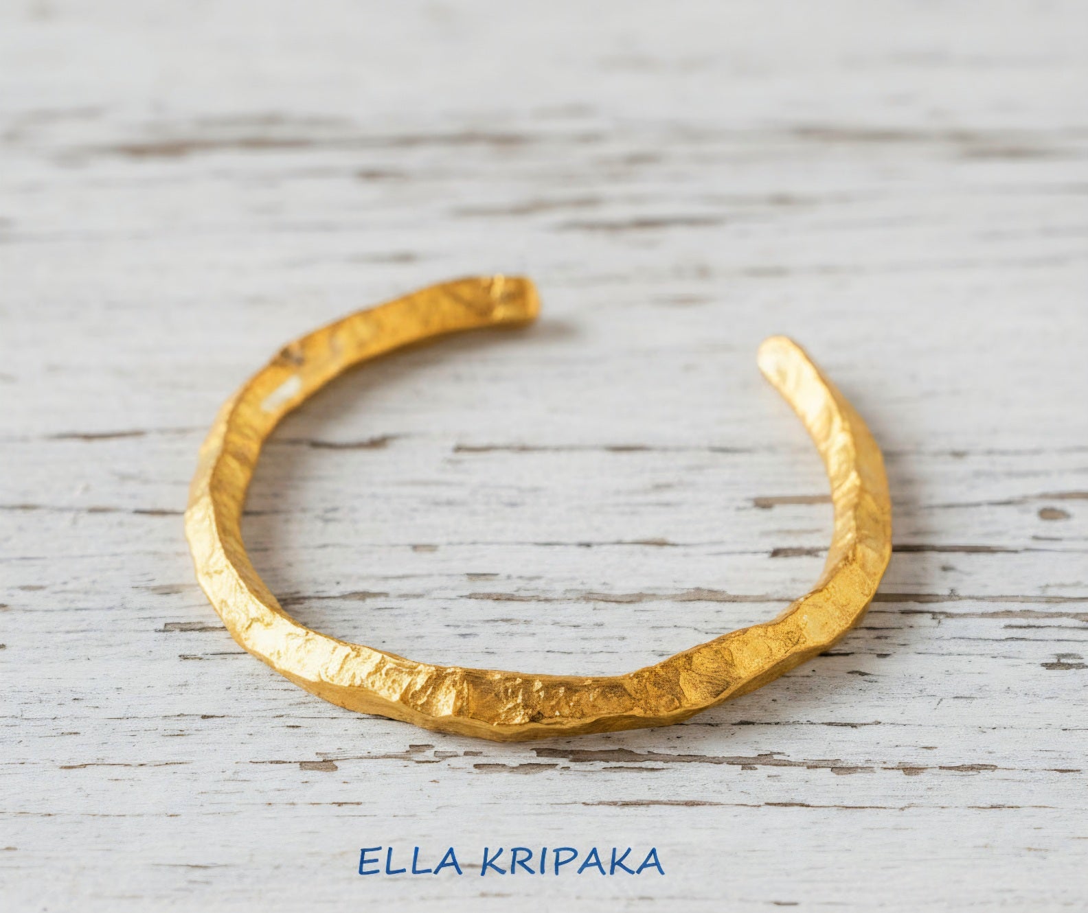 Organic hammered 24k 9999 Gold thick uneven cuff bracelet on a wooden background with 'Ella Kripaka' branding