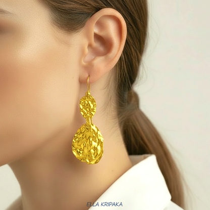 Organic 24k 9999 gold hammered wavy earrings with shiny gold textures worn by a woman and on grey background, artist-jeweler's name 'Ella Kripaka'