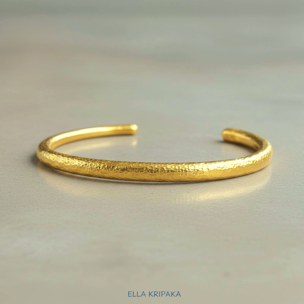 Hammered 24k 9999 gold cuff thick bracelet Ancient Rome style on a grey background, artist-jeweler name 'Ella Kripaka' branding