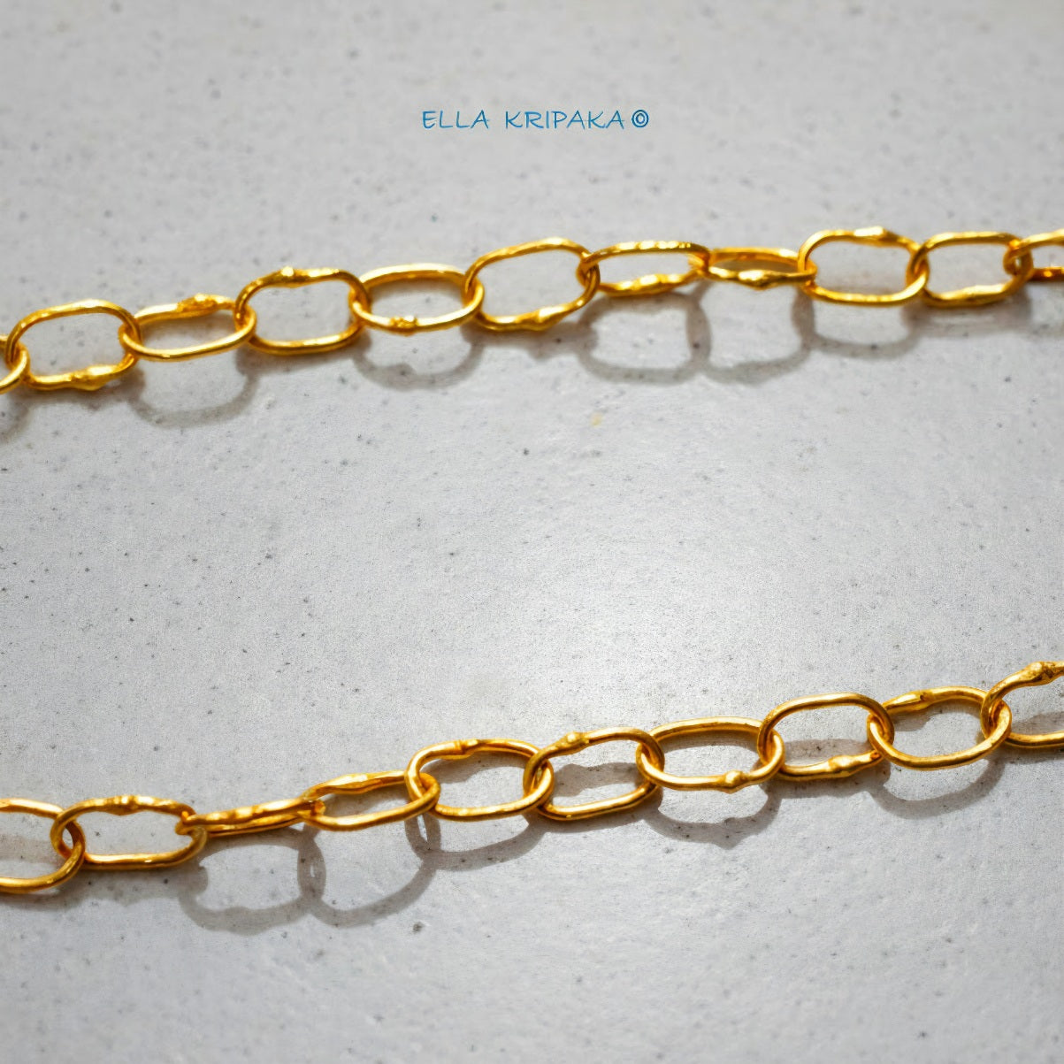 22k gold hammered chain on grey concrete background, artist-jeweler's name 'Ella Kripaka' branding