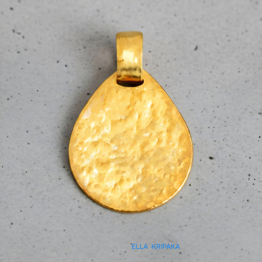 Hammered 24k gold, pure 9999 gold drop pendant with shiny forged gold textures on grey concrete surface, artist-jeweler 'Ella Kripaka' branding