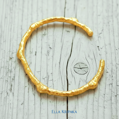 Organic hammered 24k 9999 gold bracelet uneven cuff on a old white wooden background, branding artist-jeweler name 'Ella Kripaka'